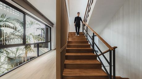 A modern staircase with wood treads and black metal railings leads to an upper level, surrounded by large windows.