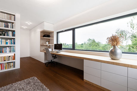 Modern and minimalist home office with sleek built-in desk, shelving, and large window overlooking greenery.