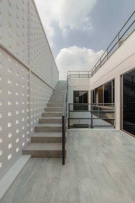 Modern architecture with concrete stairs, metal railings, and patterned walls leading to open outdoor space.
