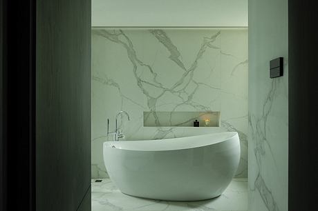 A modern bathroom with a freestanding, oval-shaped white bathtub and a marble-patterned wall.