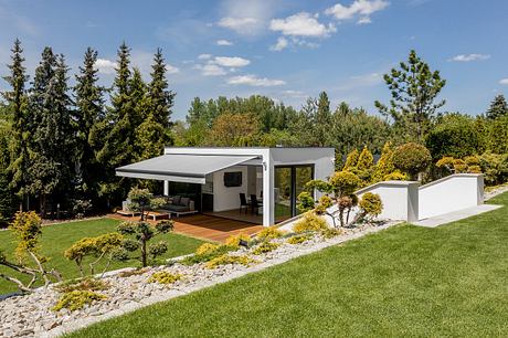 Modern, single-story home with covered patio, surrounded by lush gardens and mature trees.