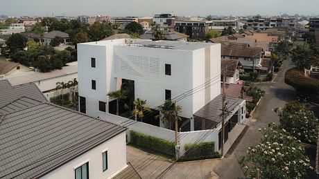 Large, modern white building with perforated exterior, surrounded by trees and smaller structures.