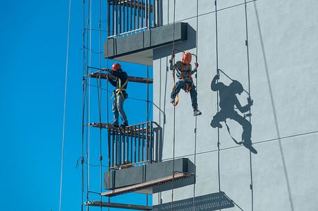 Construction workers performing repairs on the exterior of a modern building with suspended platforms and safety equipment.